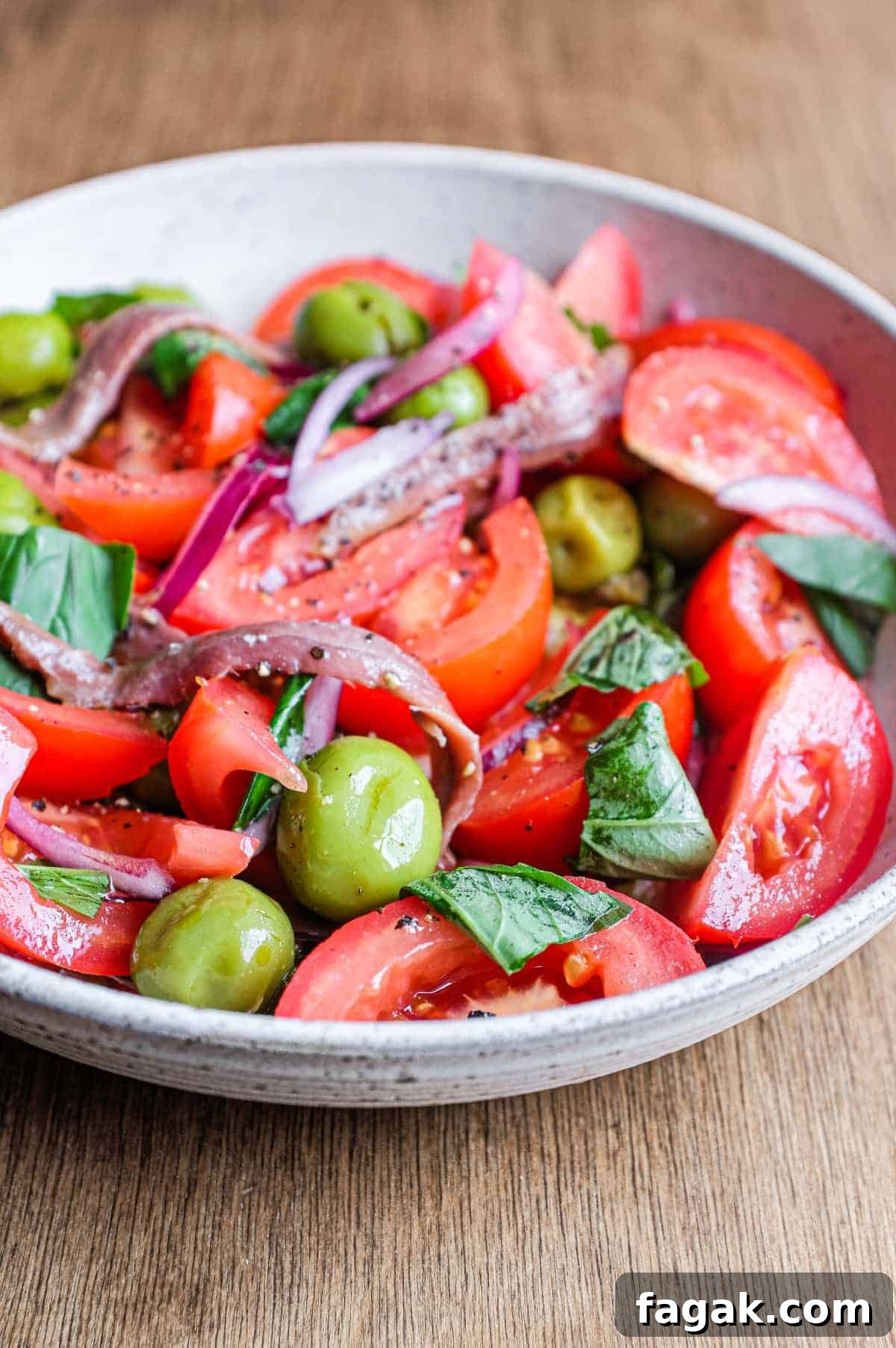 A bowl of Tomato salad with olives, capers, red onion, anchovies and fresh basil.