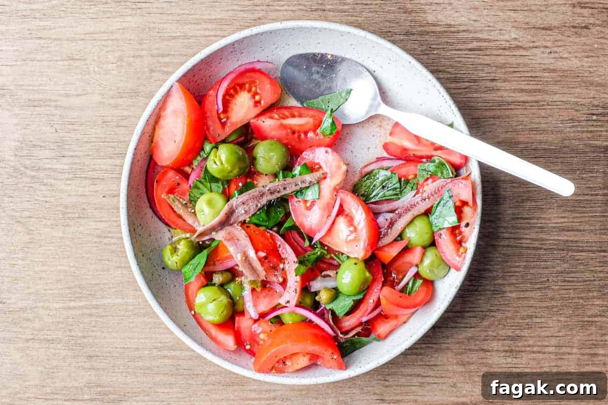 A bowl of Tomato salad with olives, capers, red onion, anchovies and fresh basil.