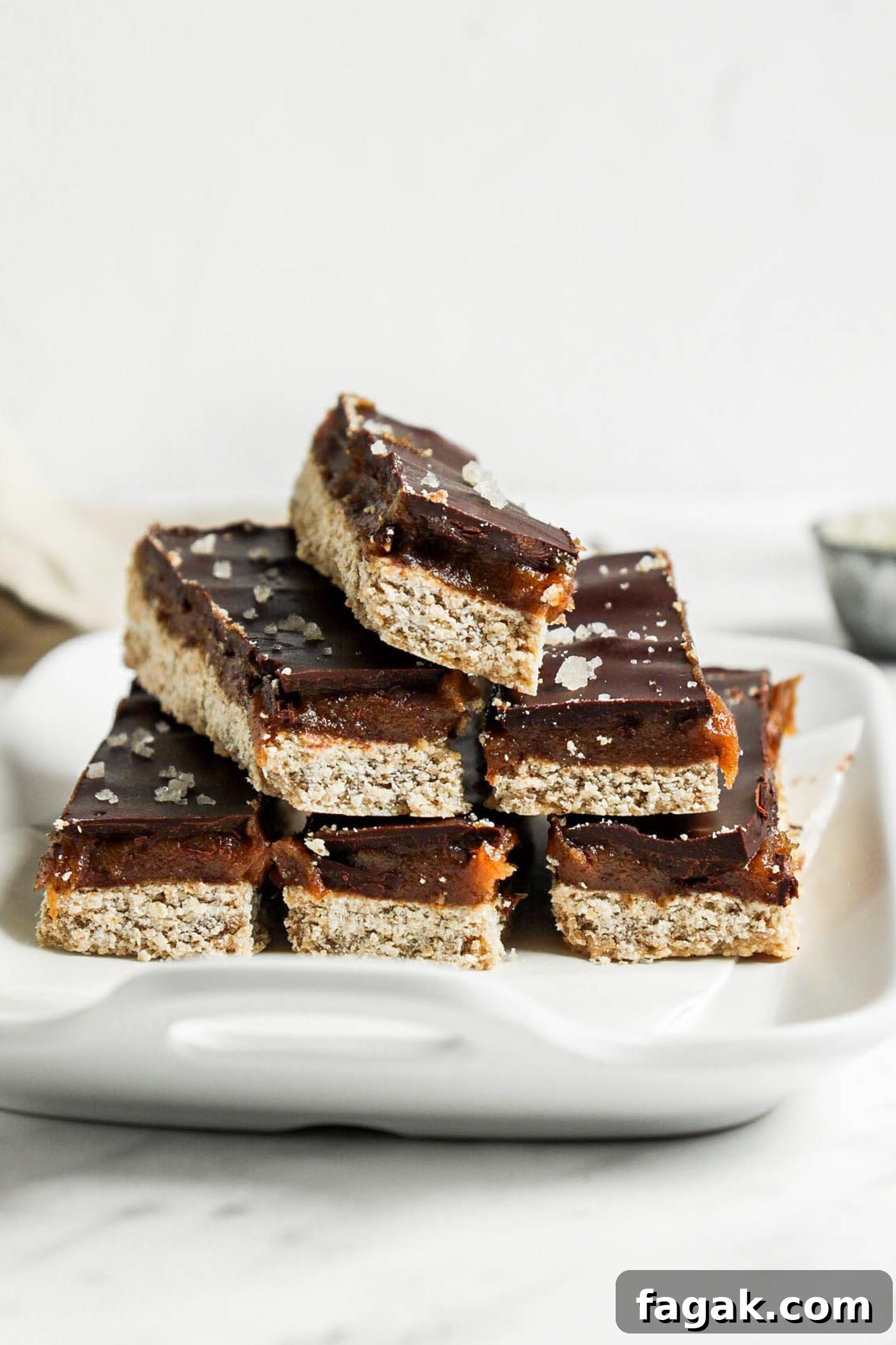 Stack of 6 homemade Twix-style bars with a shortbread, caramel and chocolate layer on a small dish.