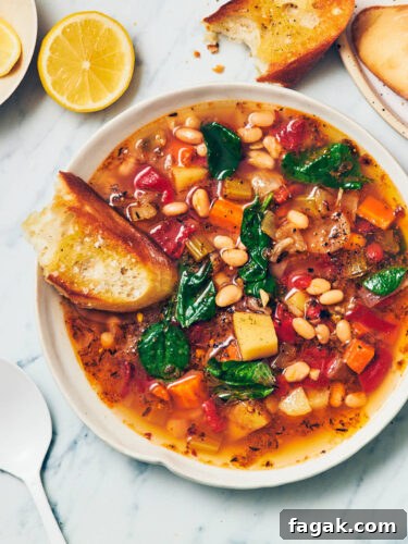A bowl of Instant Pot Navy Bean Soup with a piece of bread sitting on the edge of the bowl, with a white spoon and sliced lemon