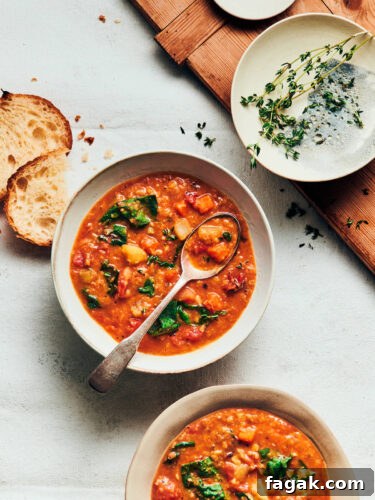 Two bowls of vegan red lentil soup on a white linen table with sourdough bread and thyme on the side