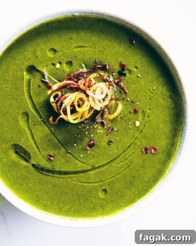 Close up of watercress soup on a white counter topped with crispy shoestring potatoes