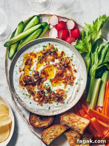 A bowl of Greek yogurt onion dip on a platter with fresh vegetables, bread, and chips for serving