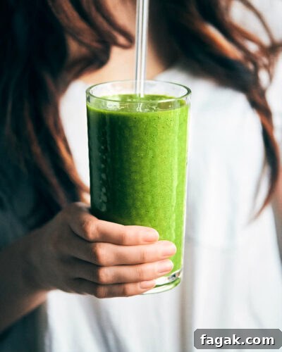 Side view of holding green smoothie with glass straw