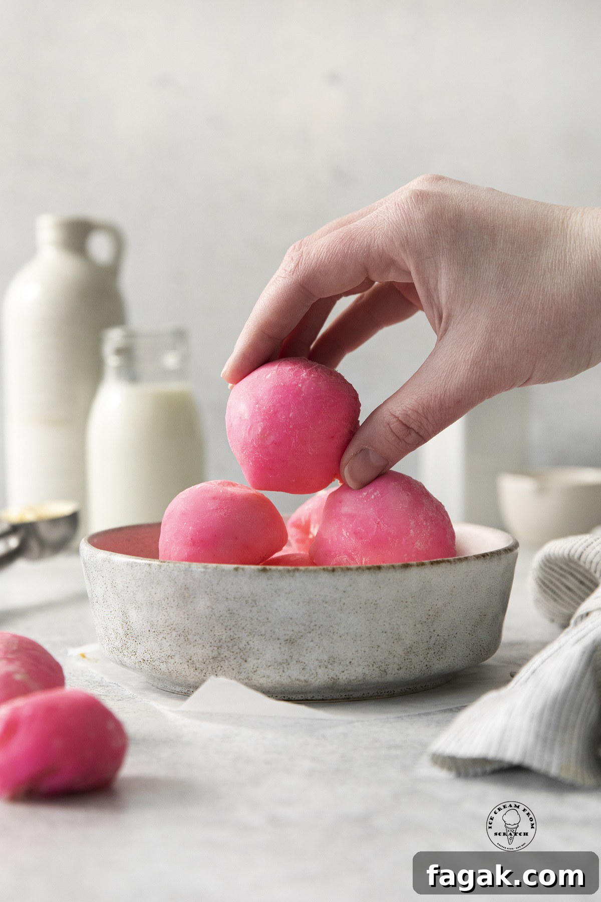 a hand picking up a pink mochi from a bowl