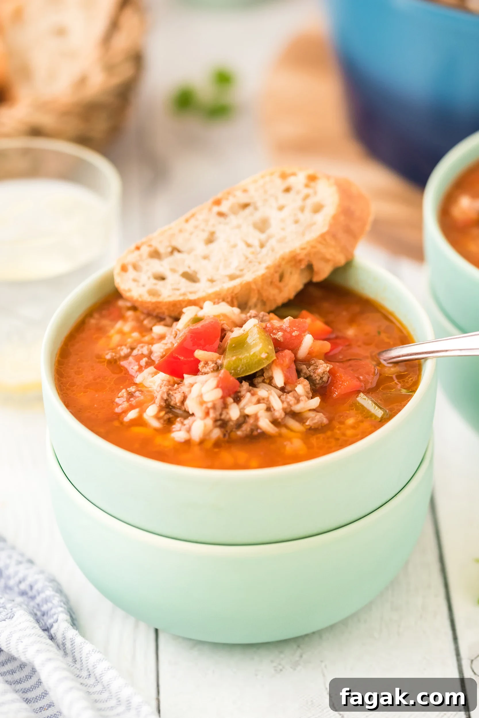 a mint green bowl of soup with a chunk of crusty bread on the rim of the bowl