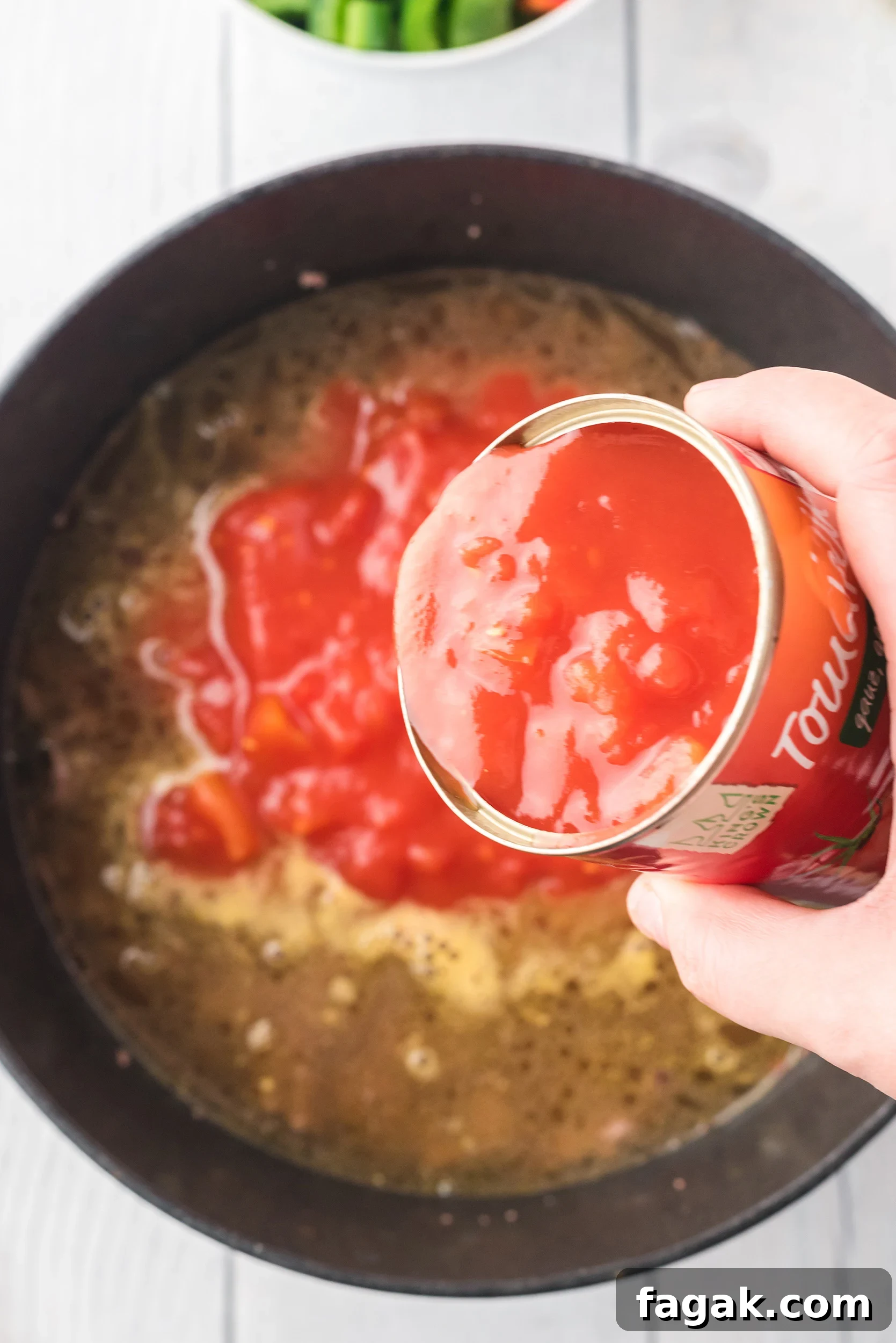 diced tomatoes and their liquid being added to the Dutch oven