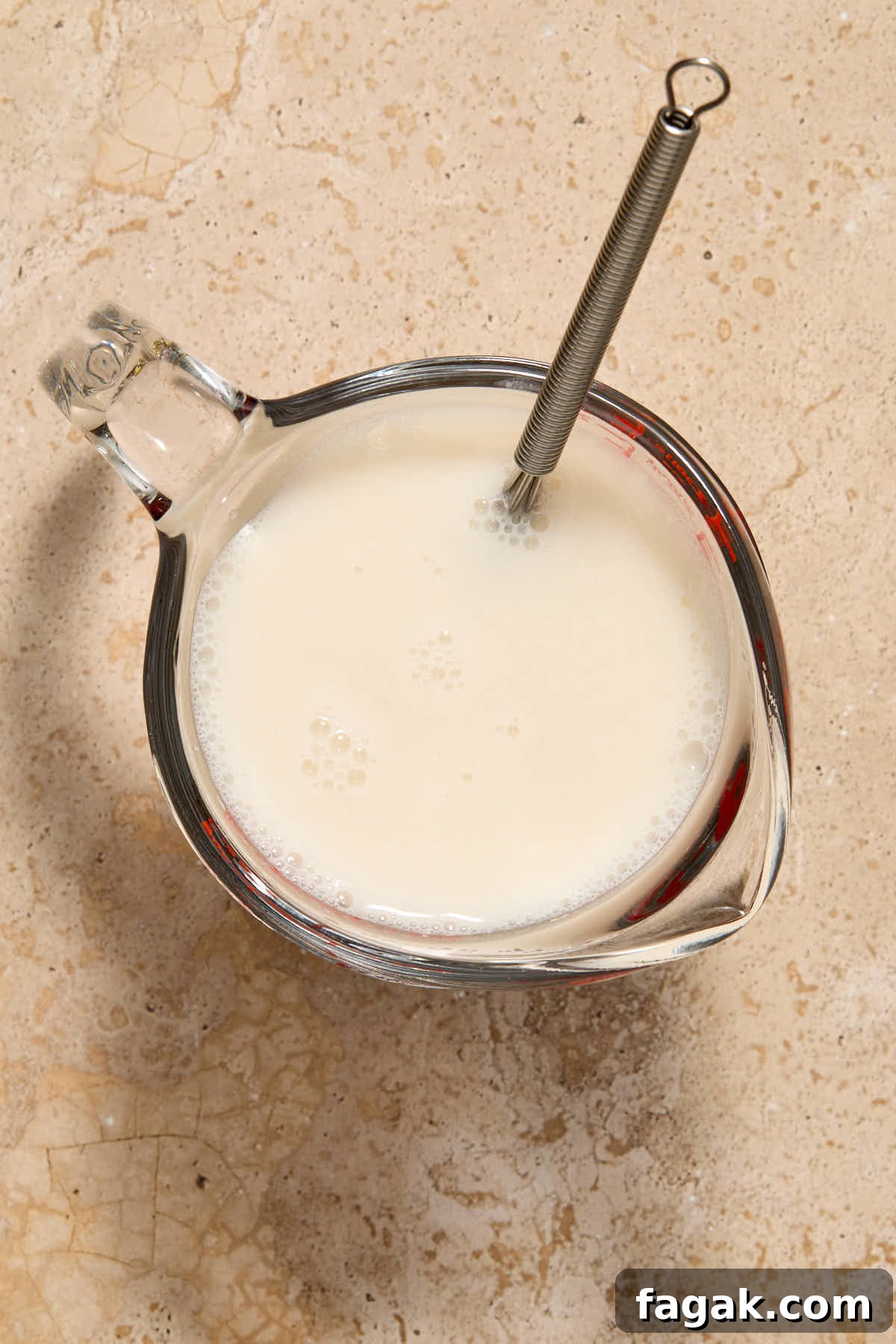 Almond milk and vinegar mixed together with a whisk in a glass measuring cup.