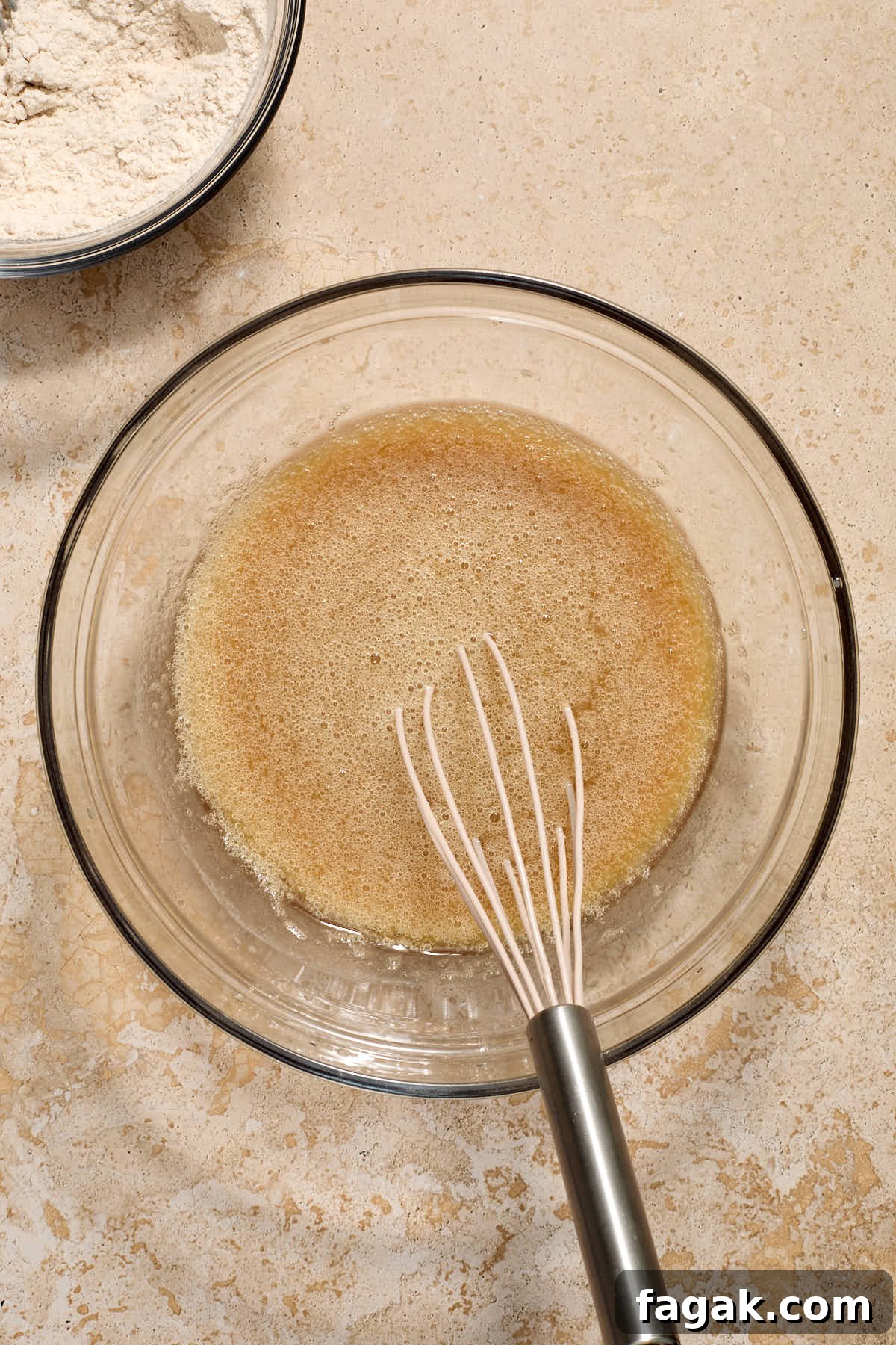 Wet ingredients whisked together in a glass bowl with dry ingredients off to the side.