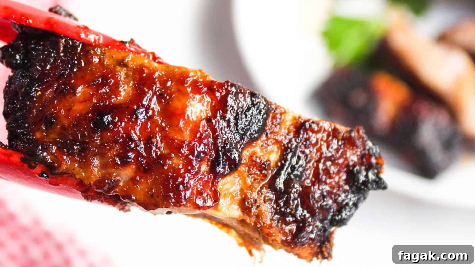 Close-up of an air-fried barbecued rib with charred edges over a white plate.