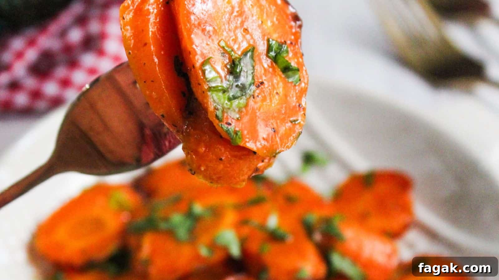 Sliced glazed carrots garnished with herbs on a fork, with more on a plate in the background.