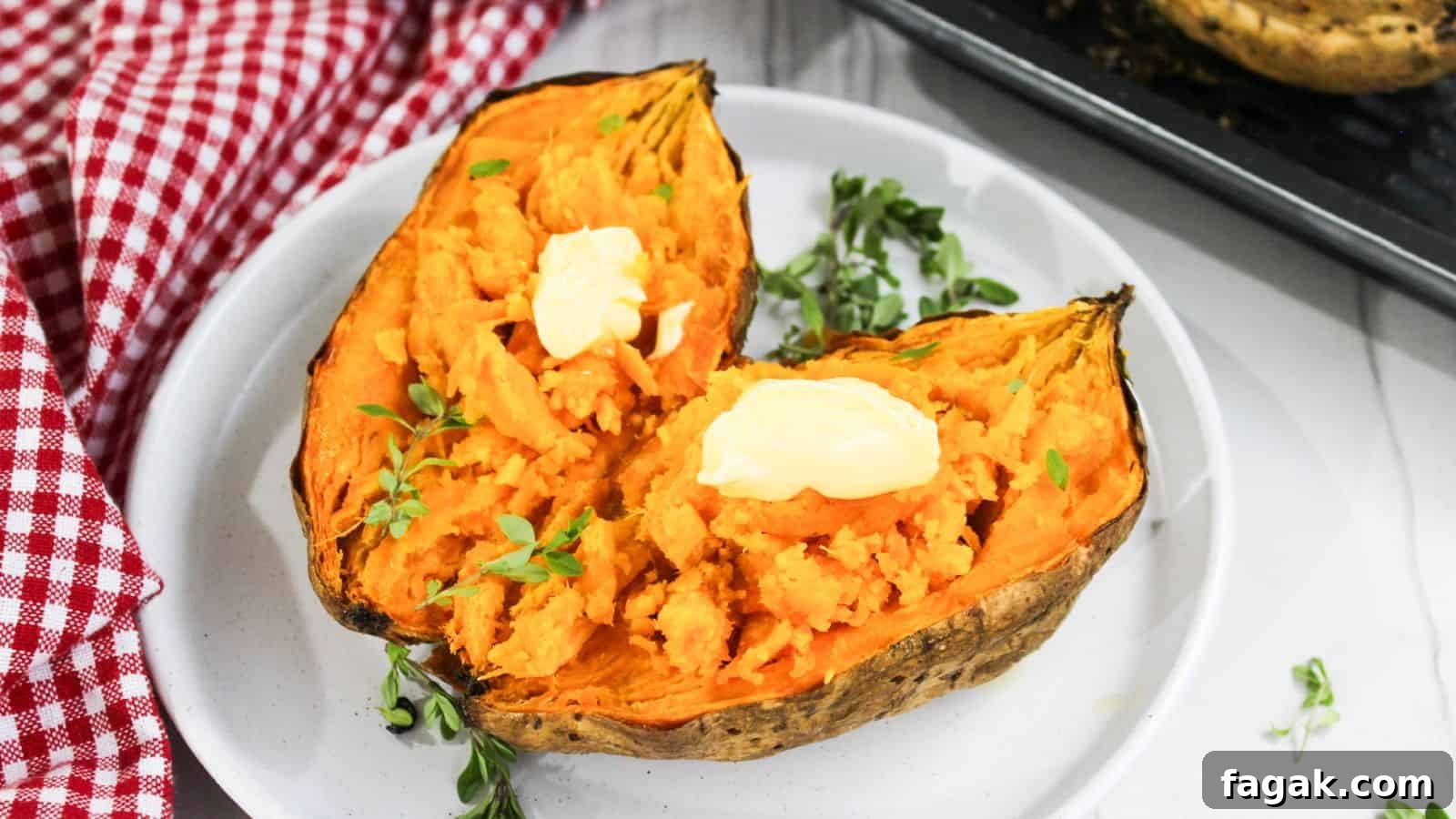 Two halves of baked sweet potato topped with butter and garnished with herbs on a white plate, with a red checkered napkin on the side.