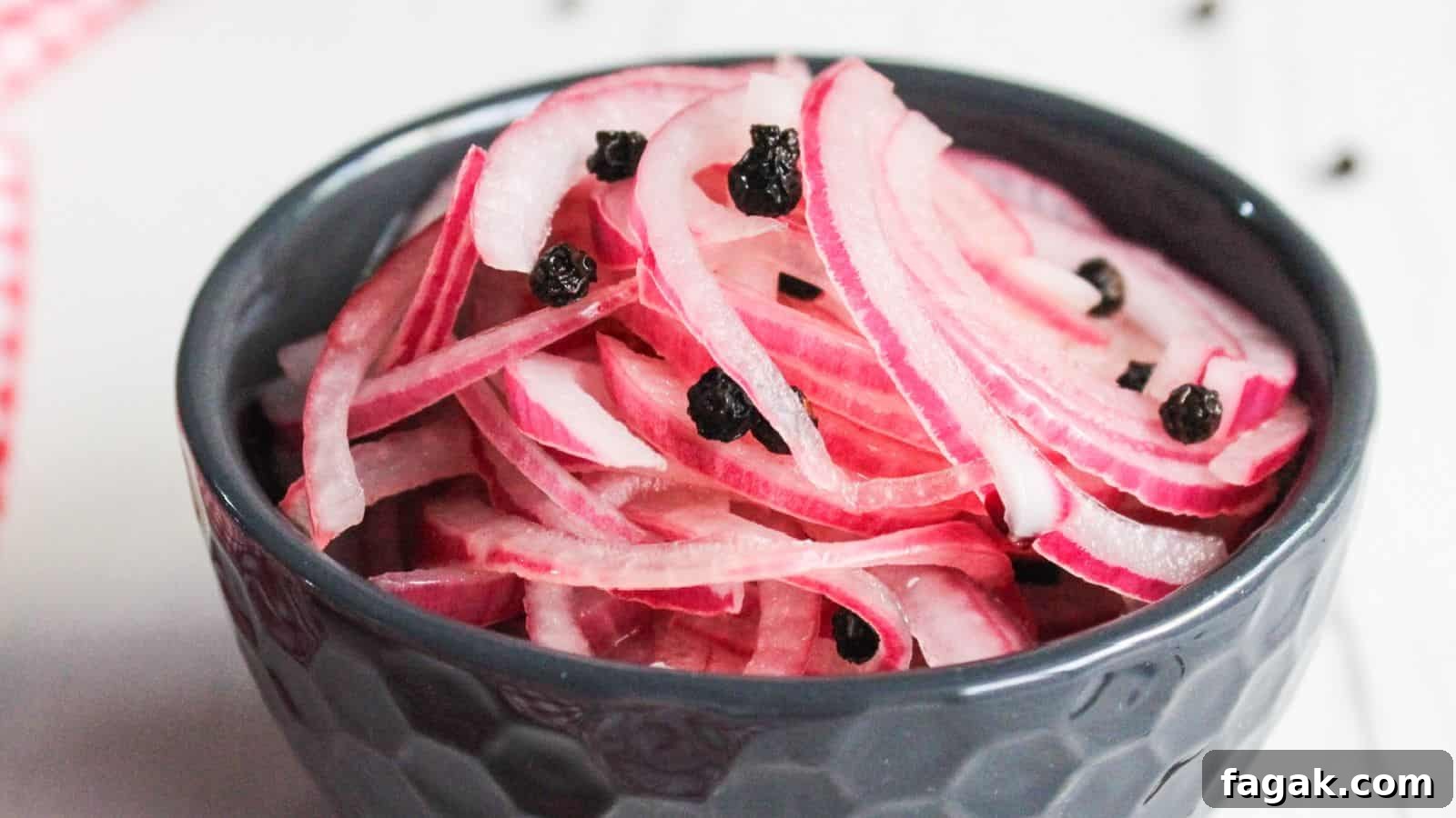 A bowl of pickled red onions garnished with black peppercorns, placed on a white surface.