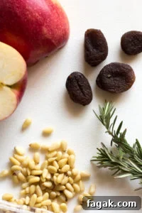 an apple, apricots, rosemary, and pine nuts on a white background