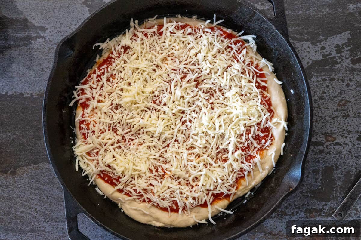pizza dough in skillet with cheese and sauce.