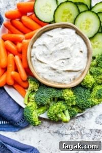 Overhead shot of ranch dip surrounded by veggies on a white plate.