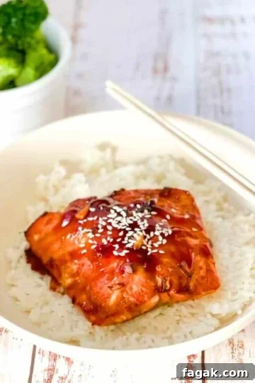 A fillet of teriyaki salmon fresh out of the air fryer on a bed of white rice, garnished with sesame seeds.