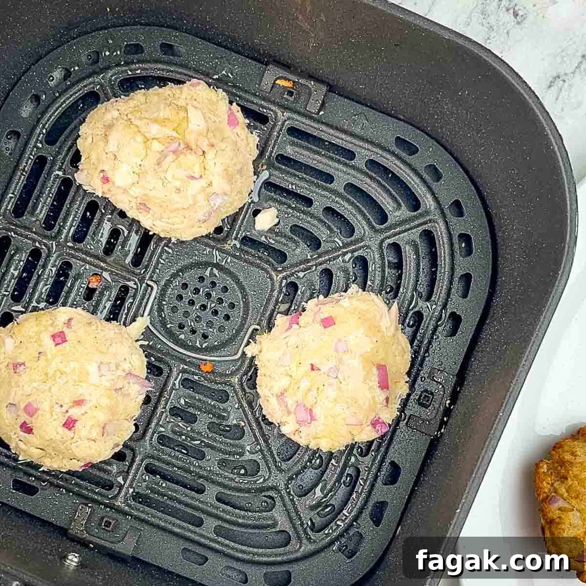 The tuna patties in a single layer of an air fryer basket.