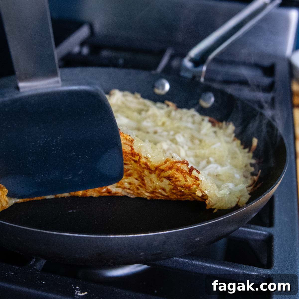 potatoes in a skillet with a spatula lifting the rosti up to see the browned underside.