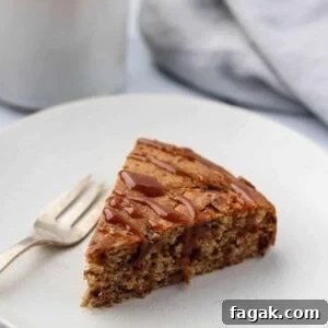A slice of date cake drizzled with caramel on a plate next to a fork and cup of coffee.