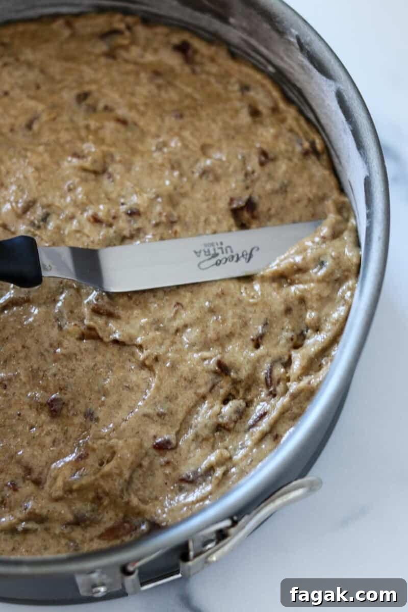 An offset spatula smoothing out the top of a cake in a pan.