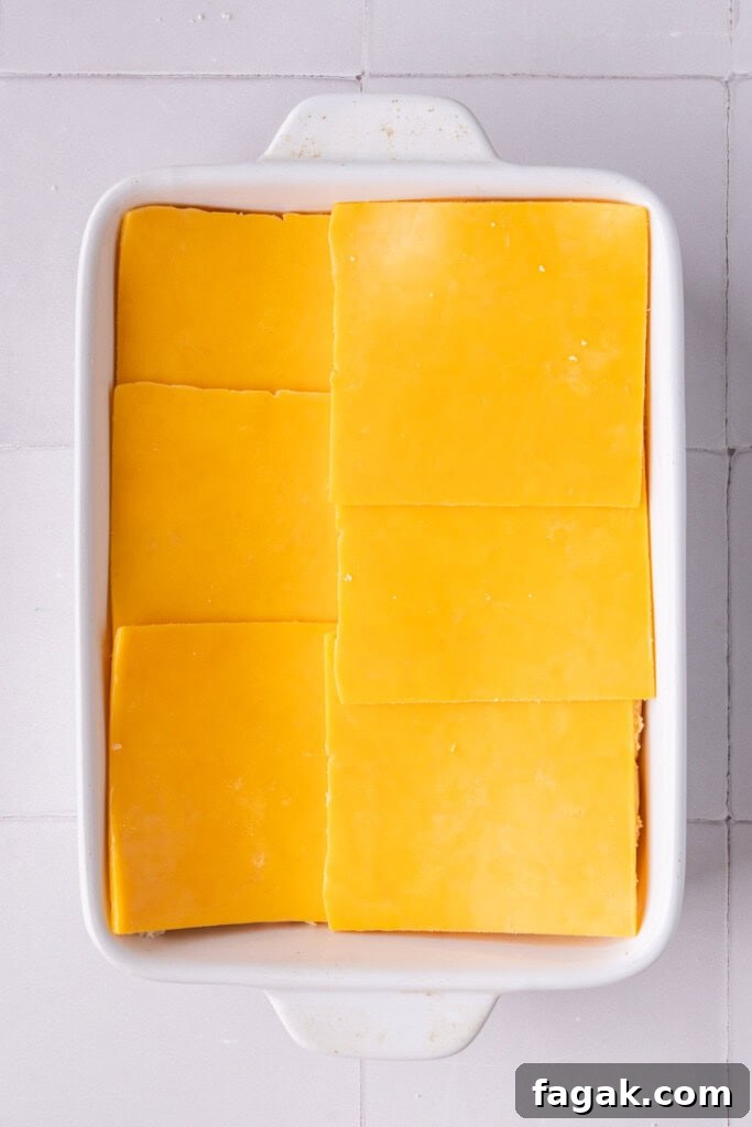 Layering cheddar cheese on top of Hawaiian rolls in a casserole dish.