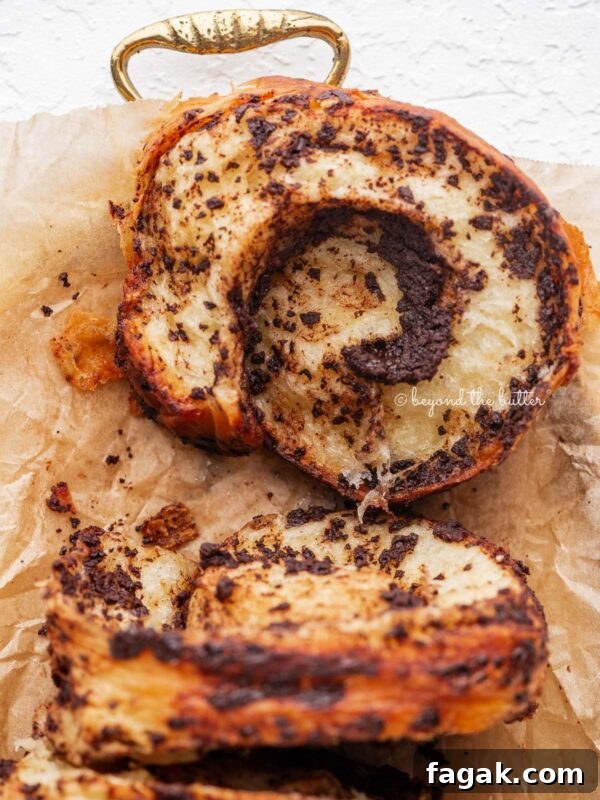 Sliced chocolate croissant loaf placed on brown parchment paper lined gold tray and white background.