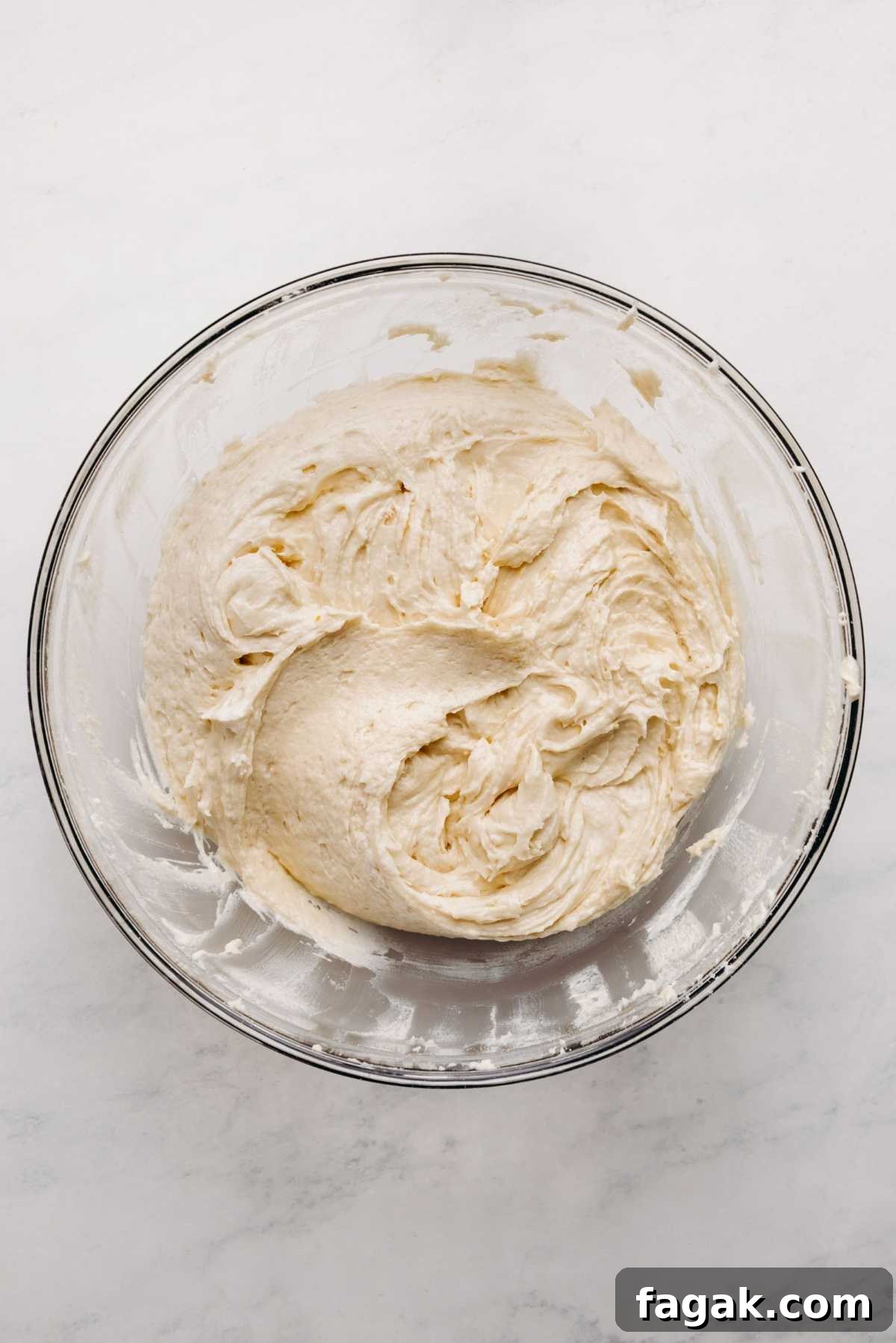 Sour cream coffee cake batter in a large glass mixing bowl on a white marbled background.