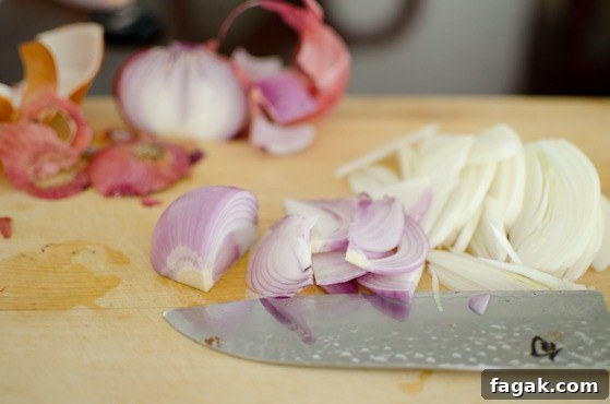 A knife is slicing white and red onion.