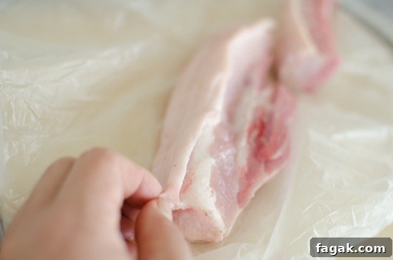 A hand is removing the outer skin of pork belly.