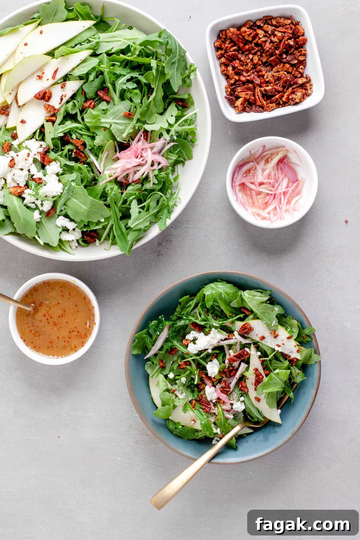 An arugula pear salad in a large bowl with a serving in a smaller blue bowl, topped with goat cheese and shallots.