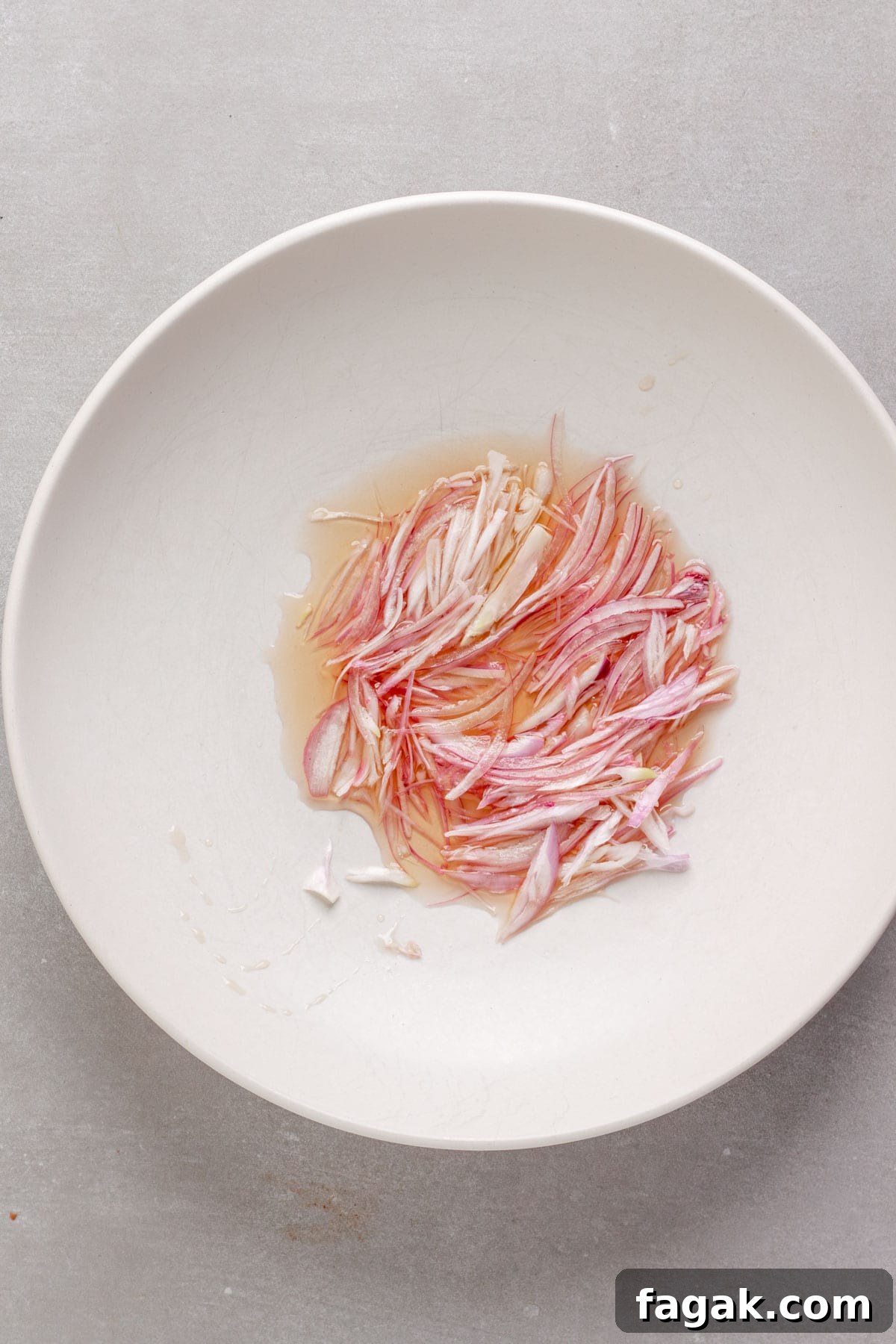 Thinly sliced shallots soaking in white balsamic vinegar in a medium bowl.