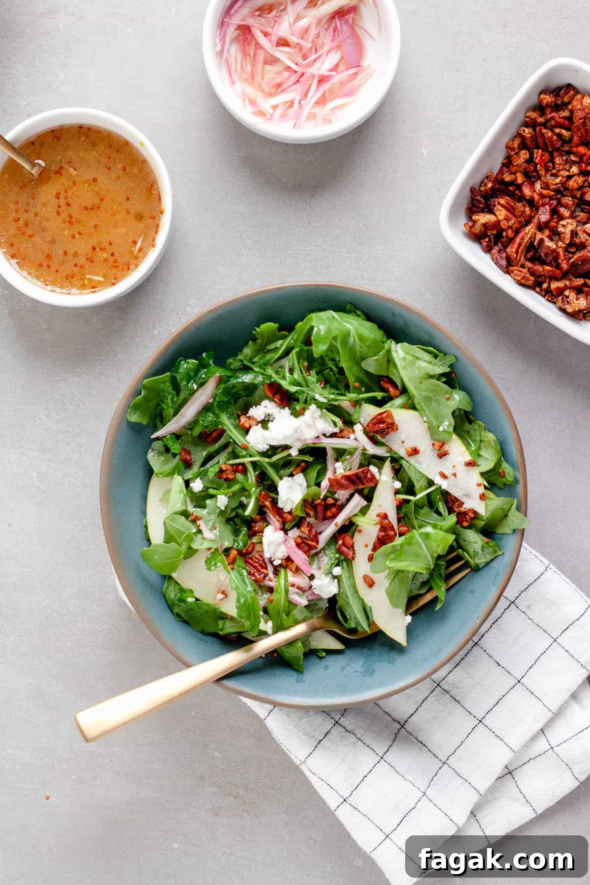 A small bowl of pear arugula salad topped with goat cheese and spiced pecans.