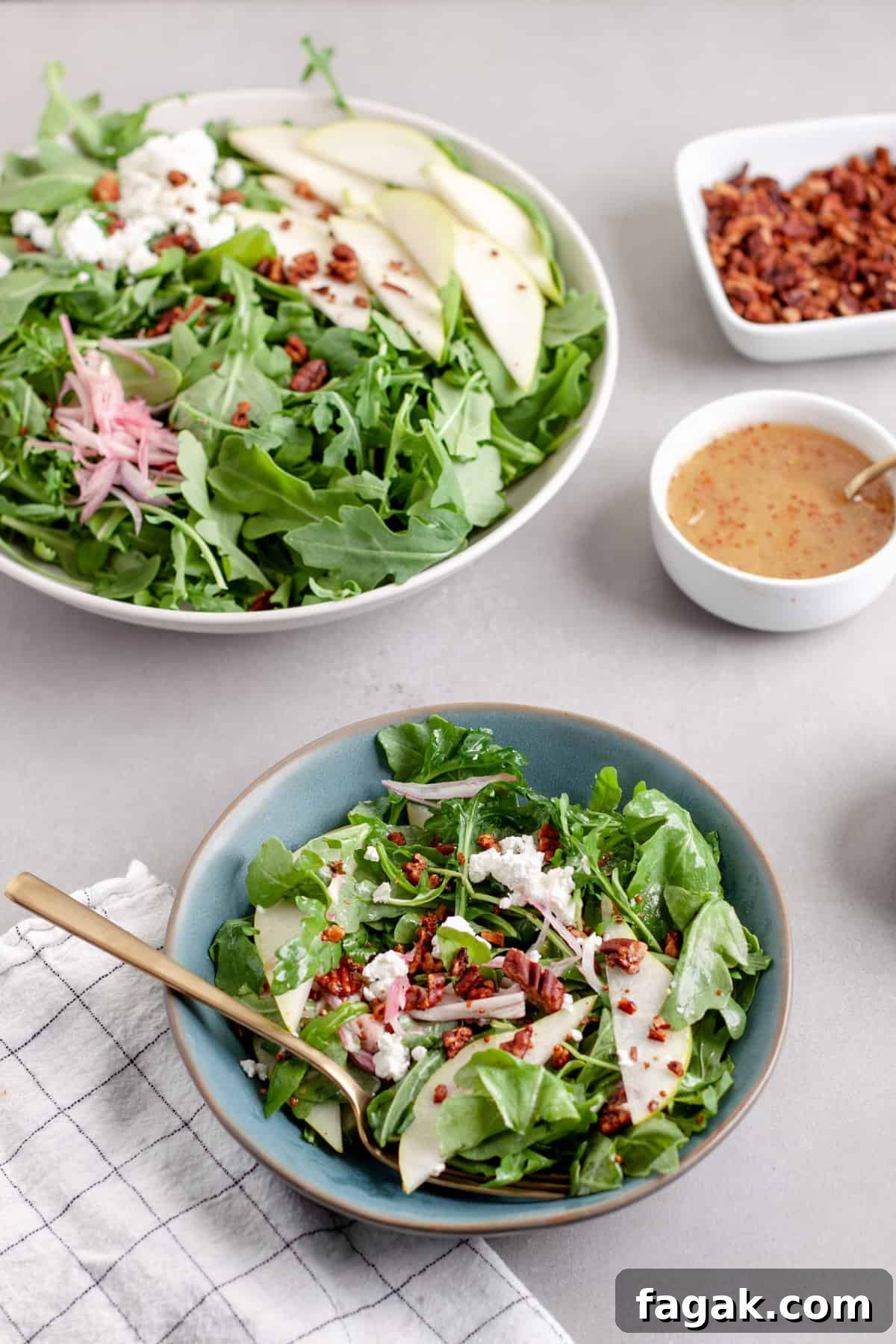 An arugula pear salad in a large bowl with a serving in a smaller blue bowl, topped with goat cheese and shallots.