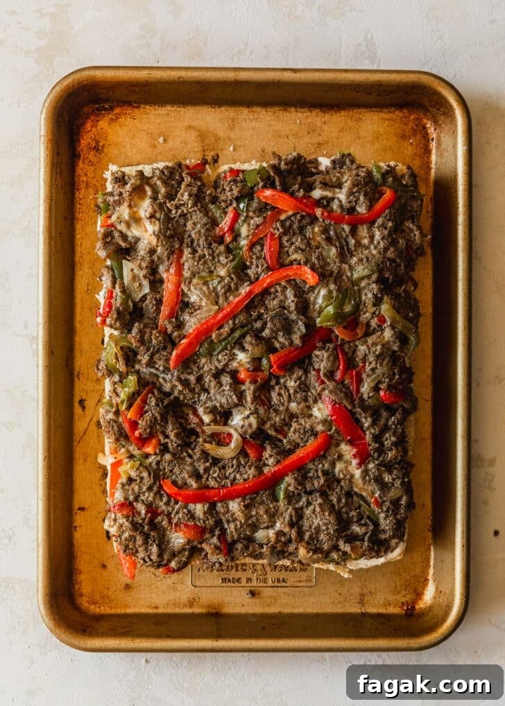 Hawaiian rolls topped with Philly cheesesteak filling on a gold sheet pan.