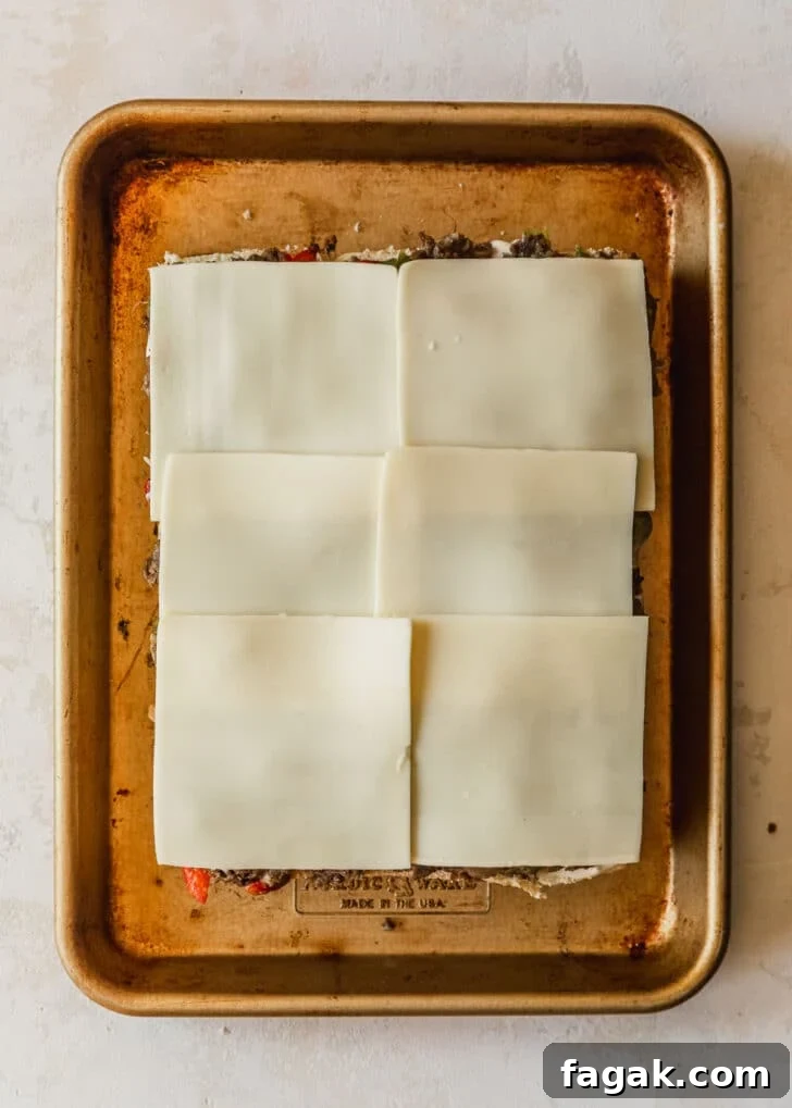Philly cheesesteak sliders topped with American cheese on a gold sheet pan.