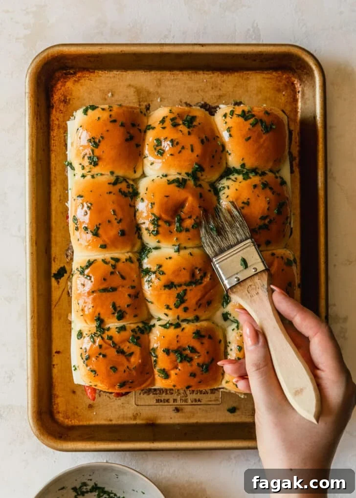 A hand brushing parsley butter over rolls on a gold sheet pan.
