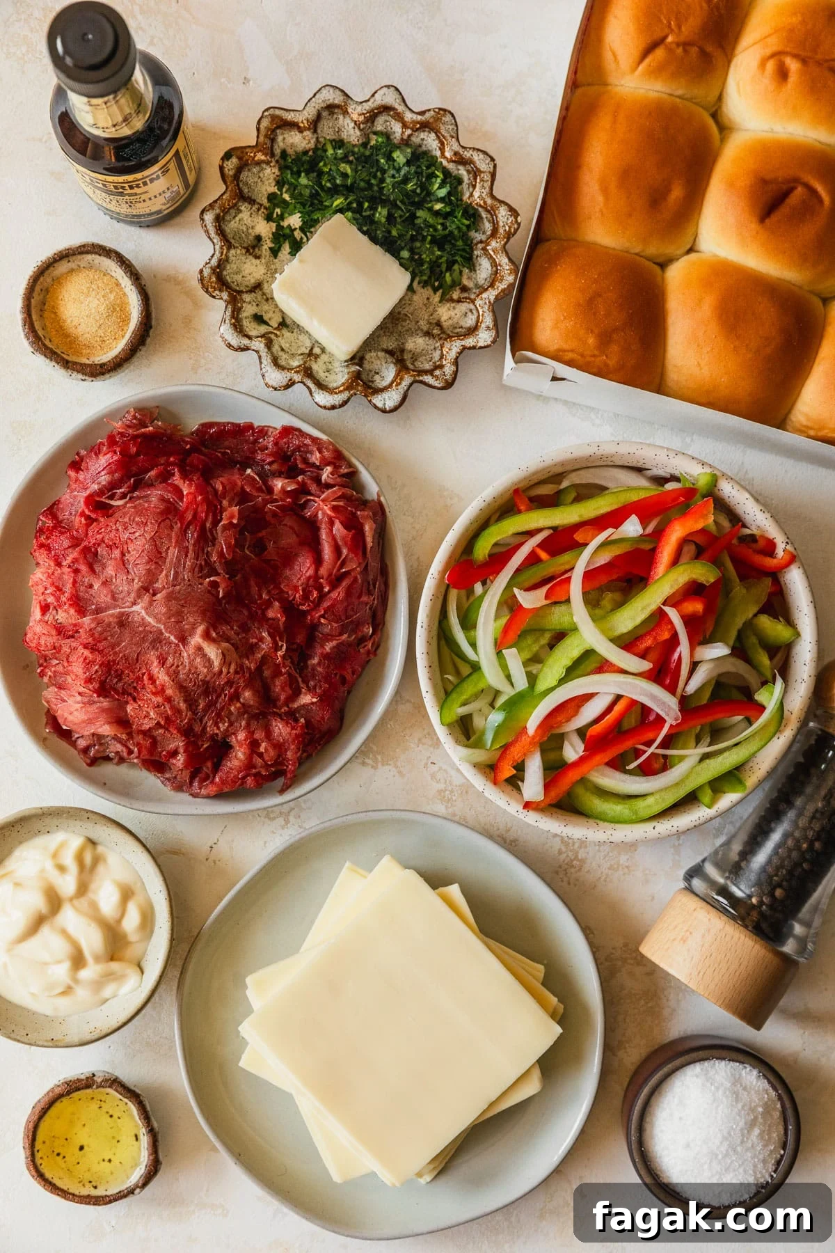 White and brown bowls of steak, peppers, onions, oil, salt, mayo, cheese, butter, parsley, and garlic powder on a tan counter next to rolls, Worcestershire sauce, and pepper.
