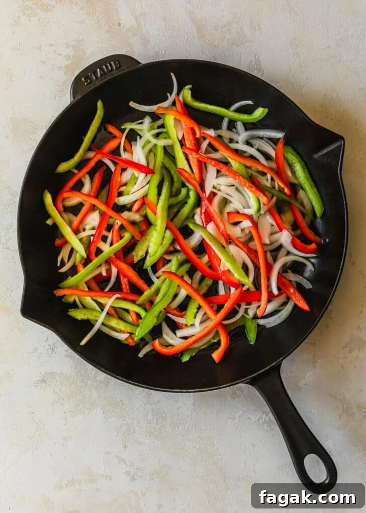 A cast iron skillet with peppers and onions on a tan counter.