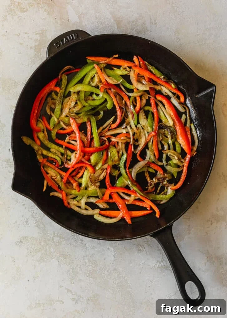 Sautéed peppers and onions in a cast iron skillet on a tan counter.