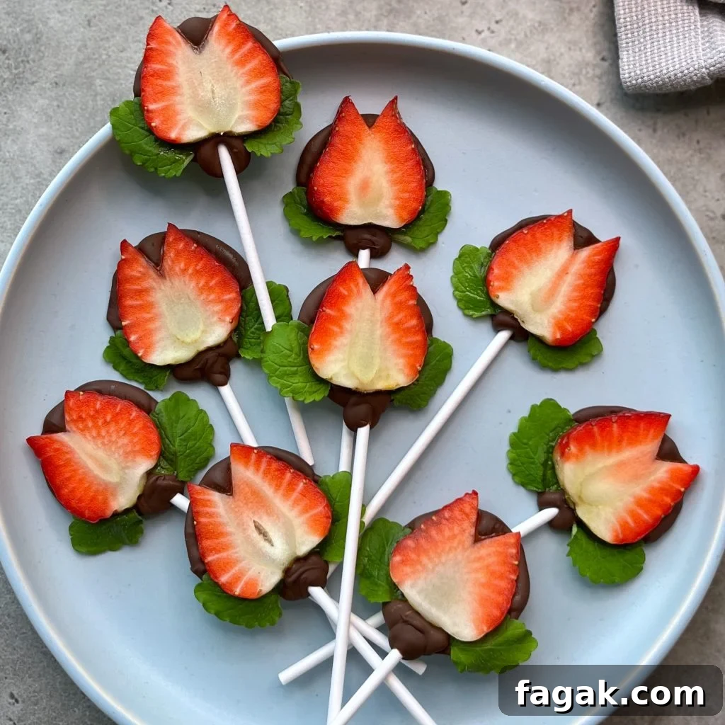 A plate with strawberry halves on sticks, dipped in chocolate and decorated with green mint leaves, arranged to resemble flowers on a blue plate—perfect for health-conscious bites or creative food recipes.