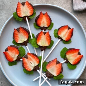 A plate displays lollipop sticks topped with halved strawberries and chocolate, arranged with green leaves to resemble edible flowers—perfect for healthy bites and creative food recipes.