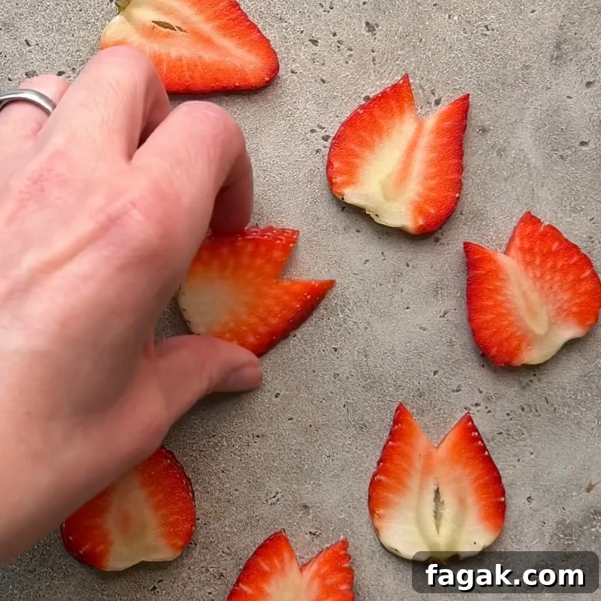 A hand arranges strawberry slices shaped like tulip flowers on a gray surface.
