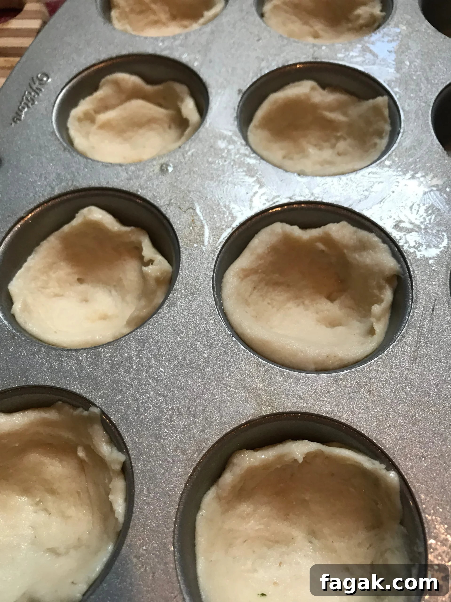 Dough pushed into cups in the muffin tin.