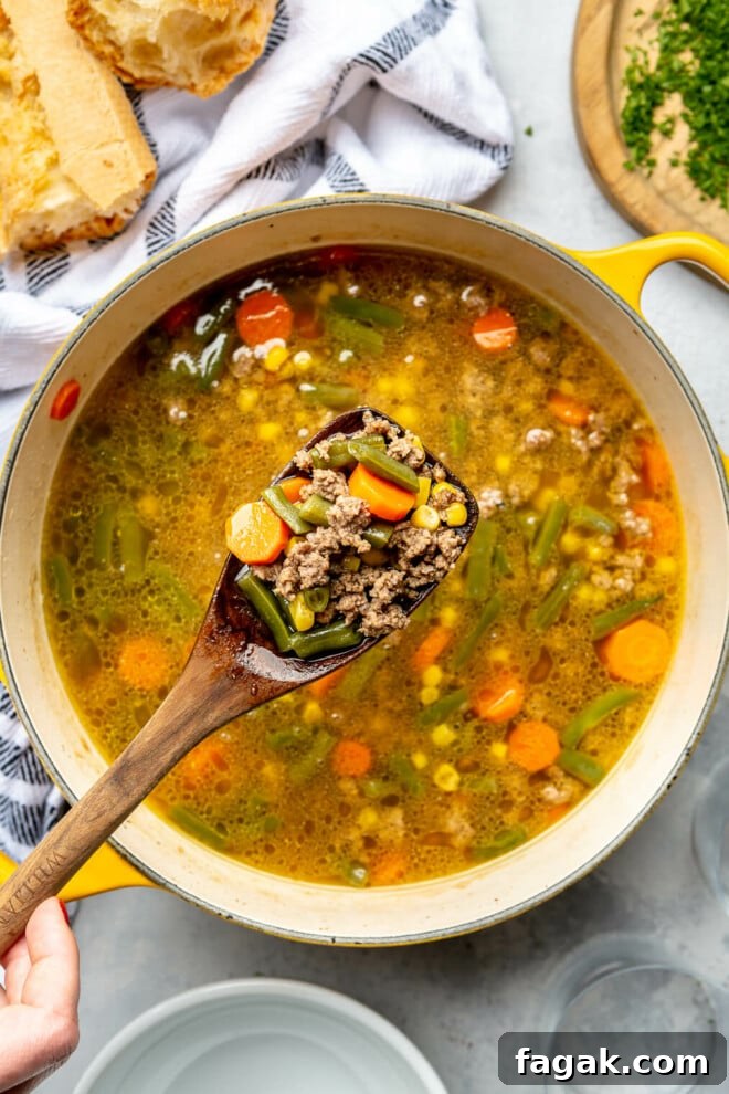 Wooden spoon with a scoop of beef vegetable soup on the spoon.