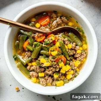 Top down view of a bowl of beef vegetable soup on a grey surface.
