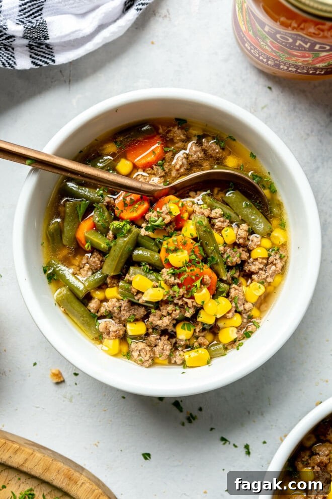 Top down view of a bowl of beef vegetable soup on a grey surface. 