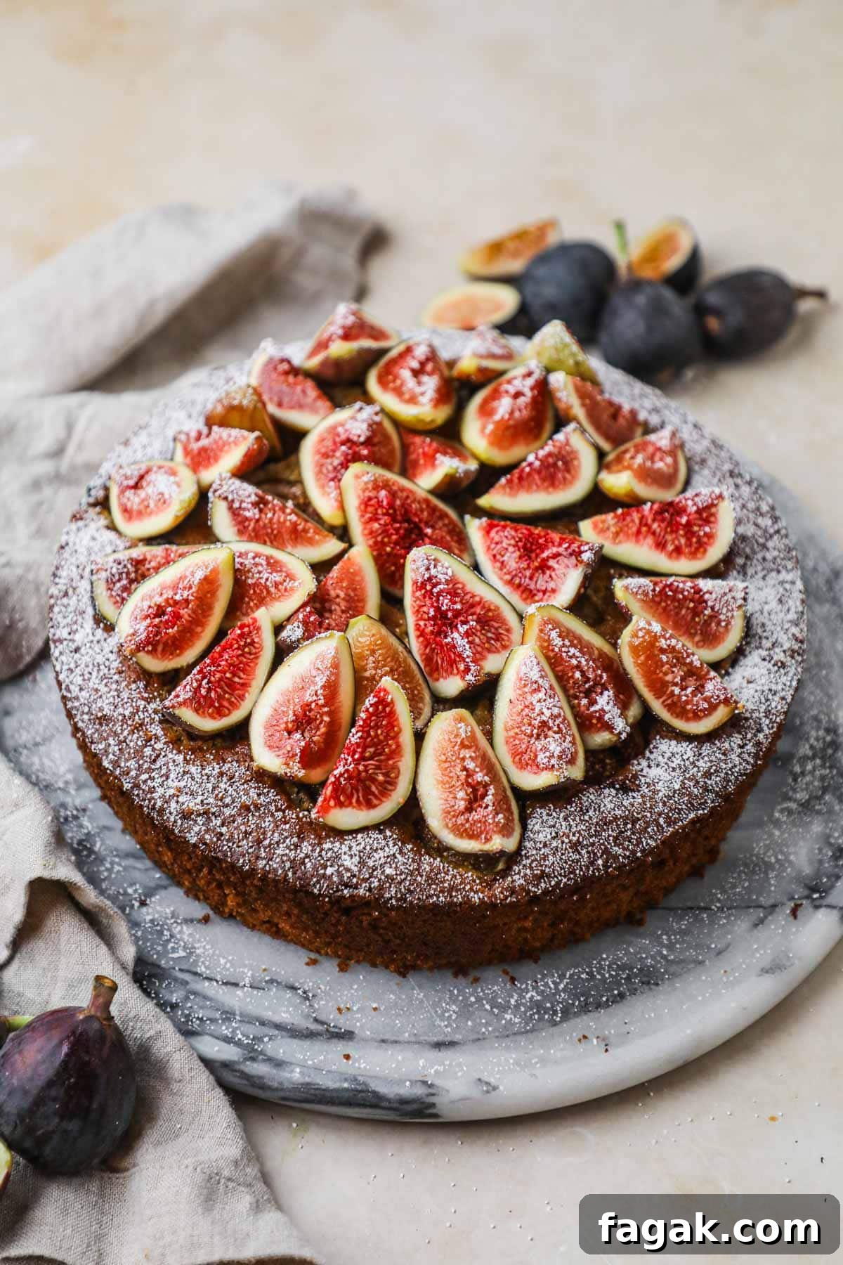 Fig and almond olive cake topped with fresh sliced figs, confectioners' sugar, and honey on a marble cake stand.