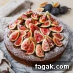 Fig and almond olive cake topped with fresh sliced figs, confectioners' sugar, and honey on a marble cake stand.