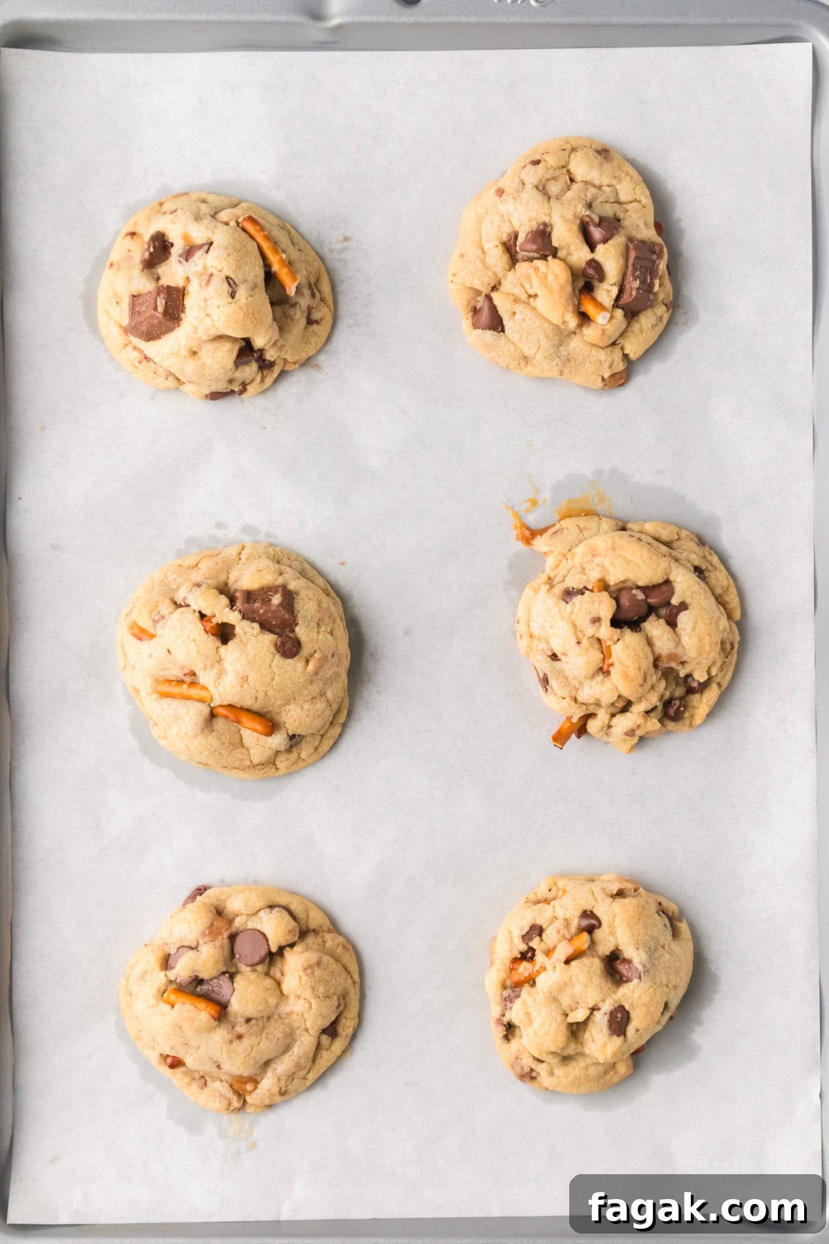 Homemade kitchen sink cookies with chocolate chunks and pretzels on lined cookie sheet.